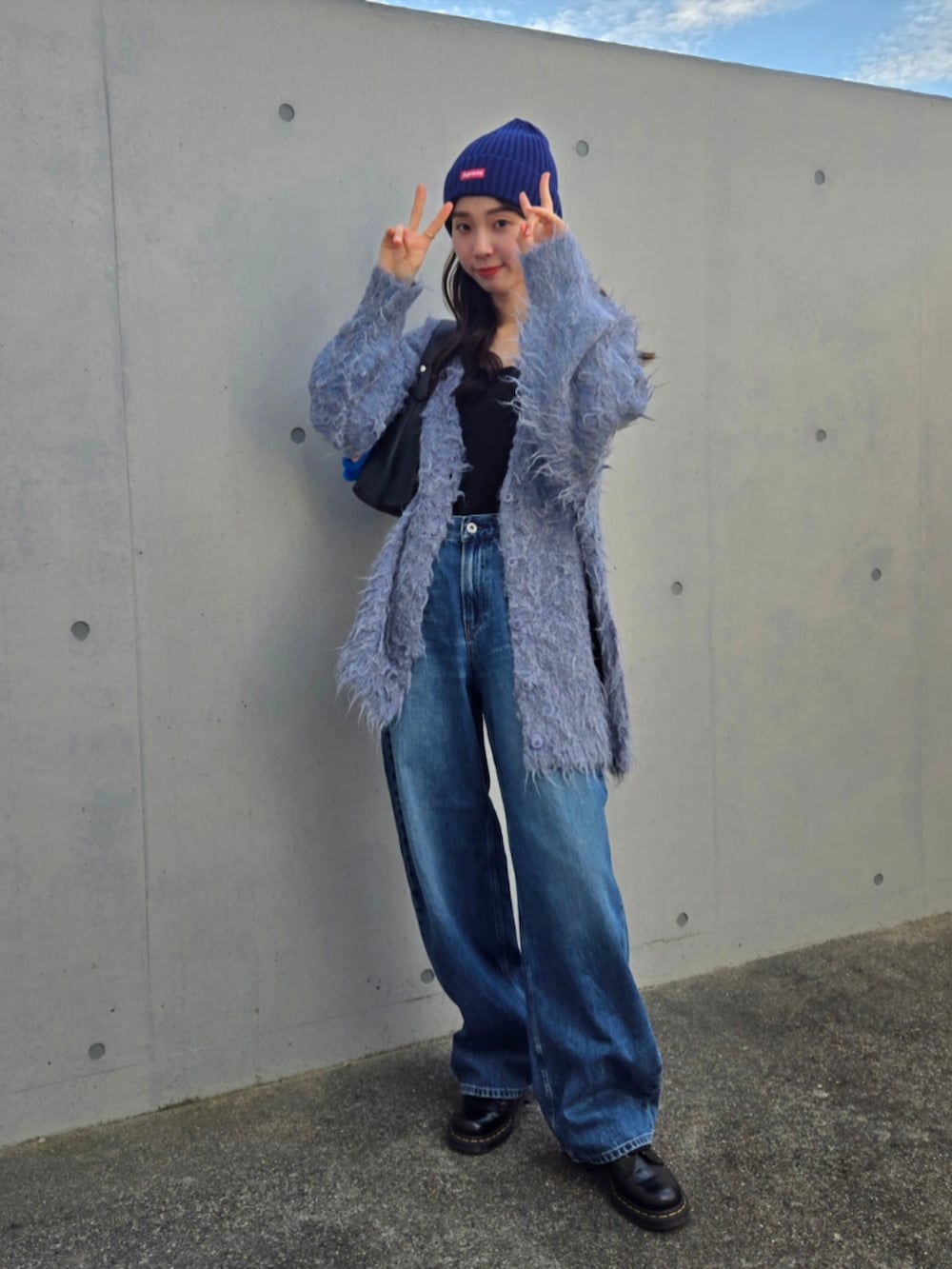 ブルー系のカーディガン/ボレロ、ブラック系のハンドバッグ、ブルー系のデニムパンツを着用したレディースの秋コーディネートの3枚目の写真