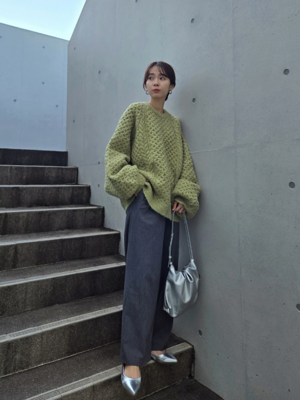 グリーン系のニット/セーター、グレー系のパンツ、シルバー系のハンドバッグを着用したレディースの秋コーディネートの4枚目の写真