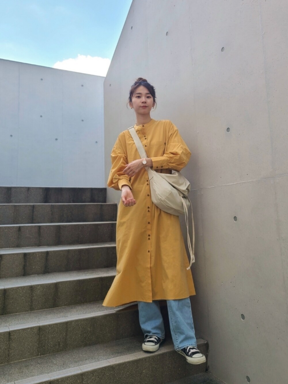 イエロー系のワンピース、ブルー系のデニムパンツ、ブラック系のスニーカーを着用したレディースの秋コーディネートの3枚目の写真