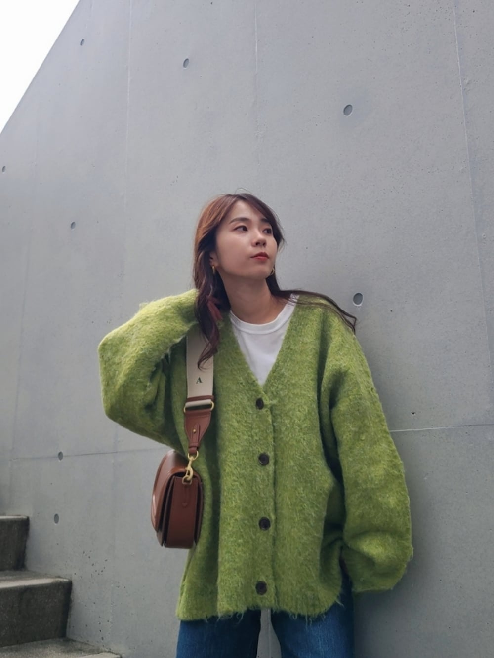 グリーン系のカーディガン/ボレロ、ブラウン系のバッグ、ブルー系のデニムパンツを着用したレディースの秋コーディネートの3枚目の写真