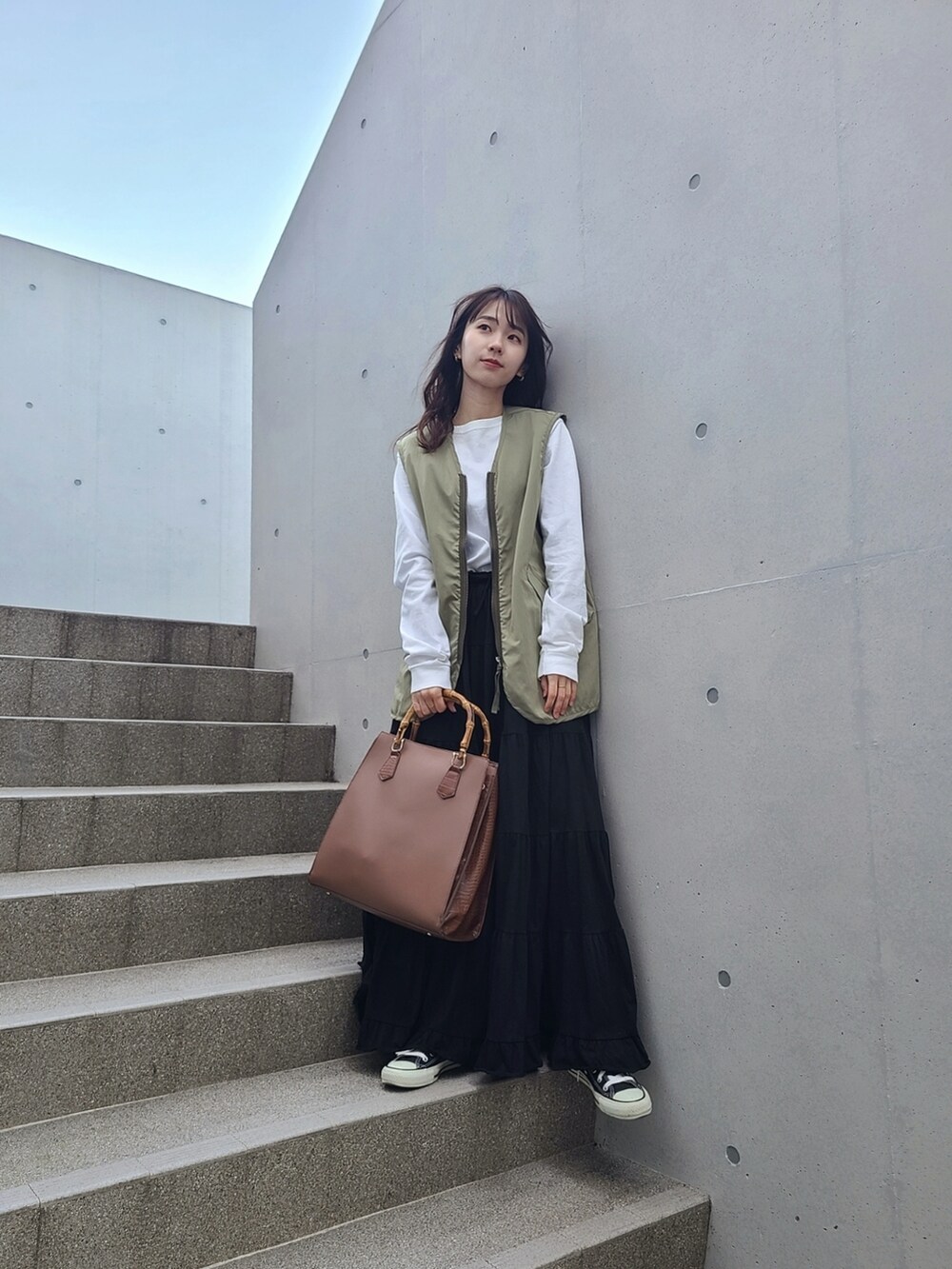 グリーン系のベスト、ブラック系のスカート、ブラック系のスニーカーを着用したレディースの冬コーディネートの2枚目の写真