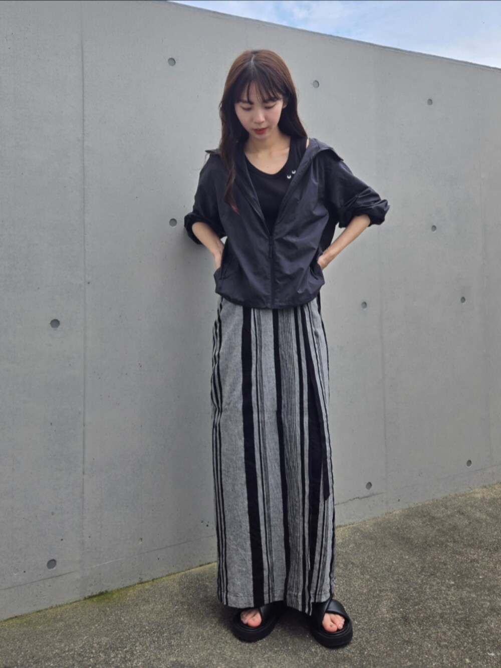 ブラック系のスカート、ブラック系のパーカー、ブラック系のサンダルを着用したレディースの夏コーディネートの3枚目の写真