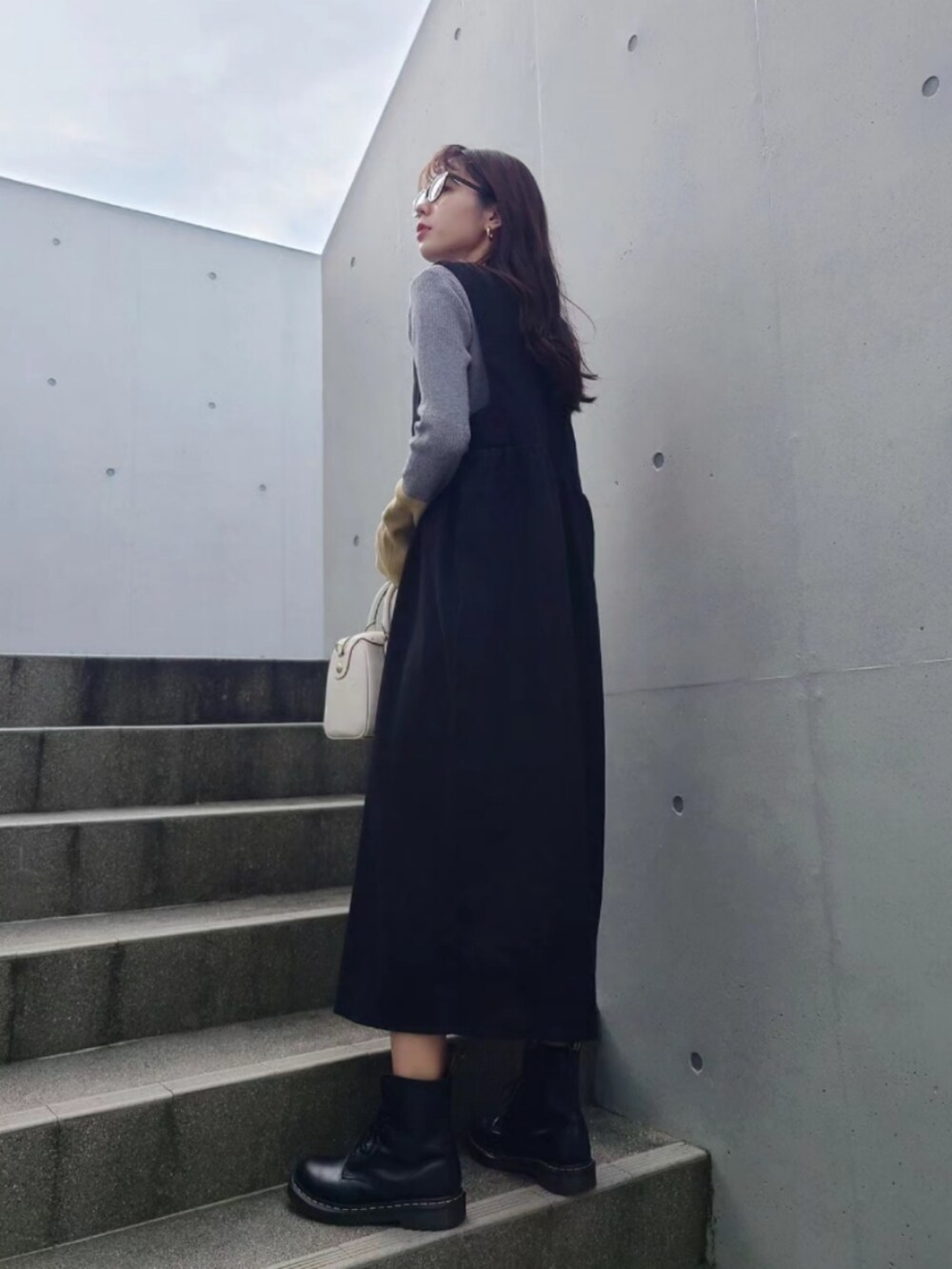 グレー系のニット/セーター、ブラック系のブーツ、ブラック系のジャンパースカートを着用したレディースの冬コーディネートの2枚目の写真