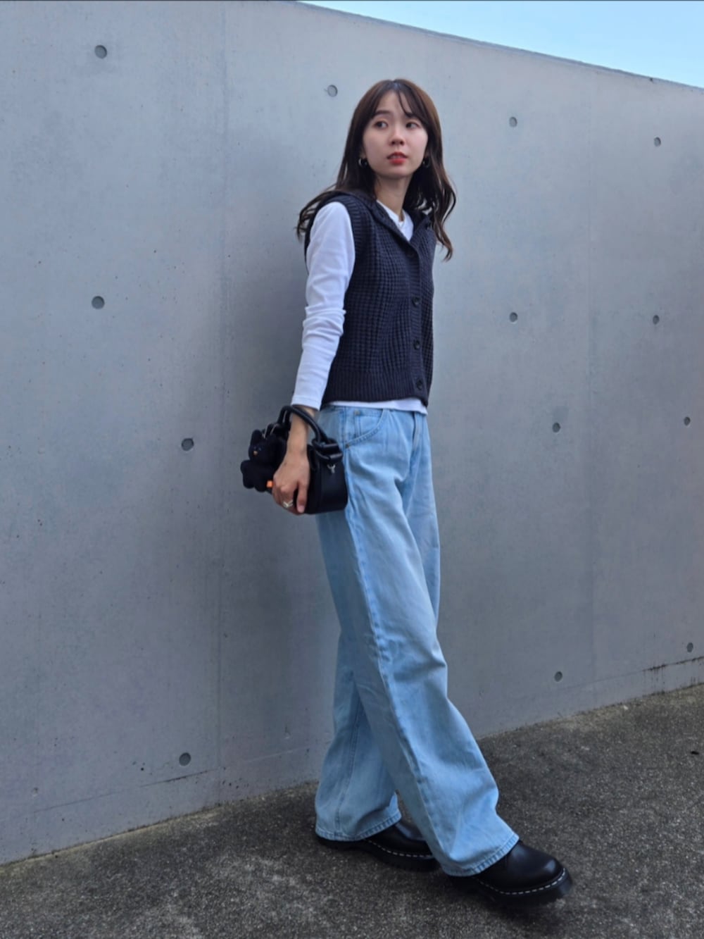 グレー系のニット/セーター、ブラック系のハンドバッグ、ブルー系のデニムパンツを着用したレディースの秋コーディネートの3枚目の写真