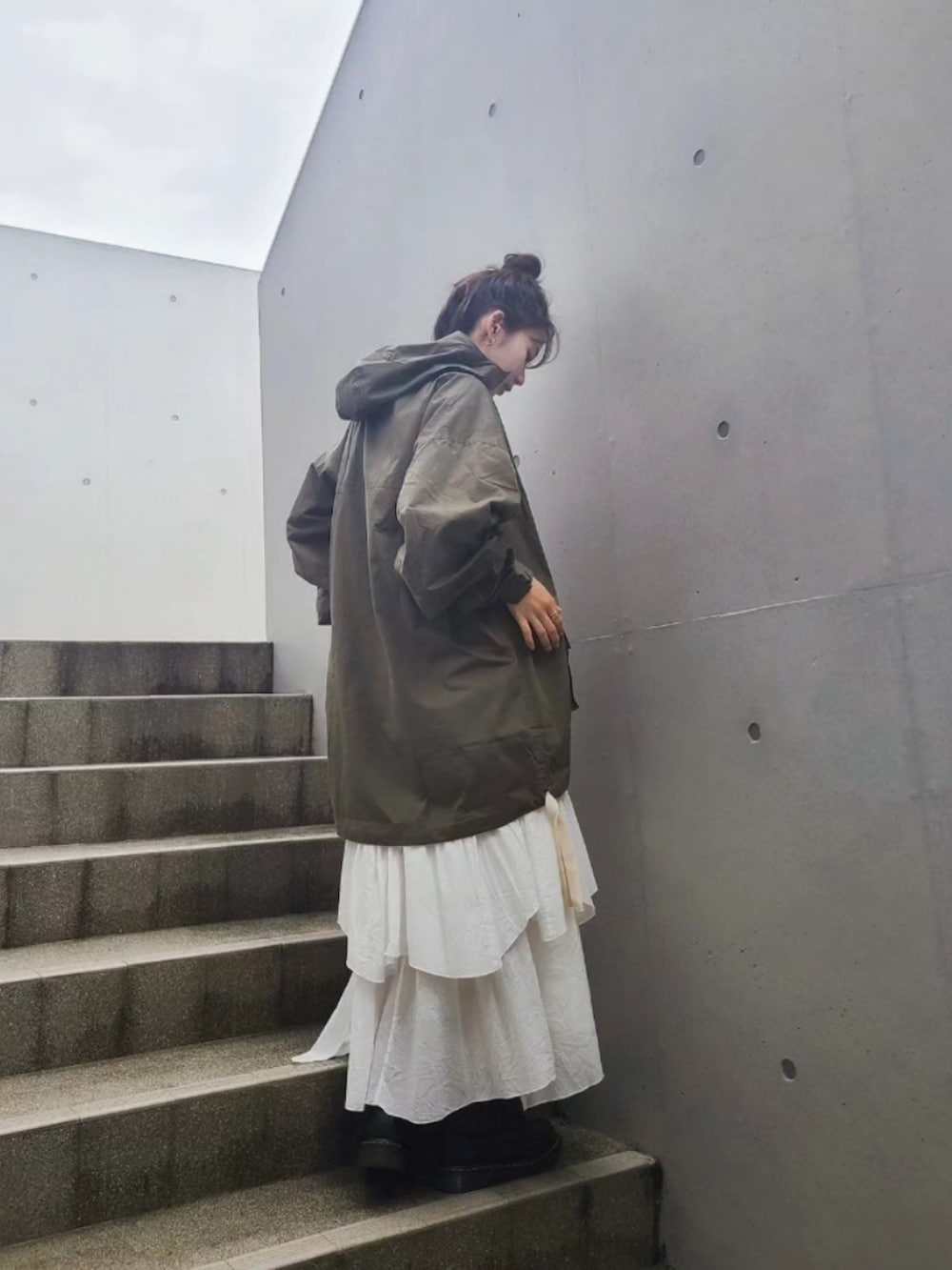 グリーン系のマウンテンパーカー、ブラック系のブーツ、ゴールド系のピアス（両耳用）を着用したレディースの夏コーディネートの2枚目の写真