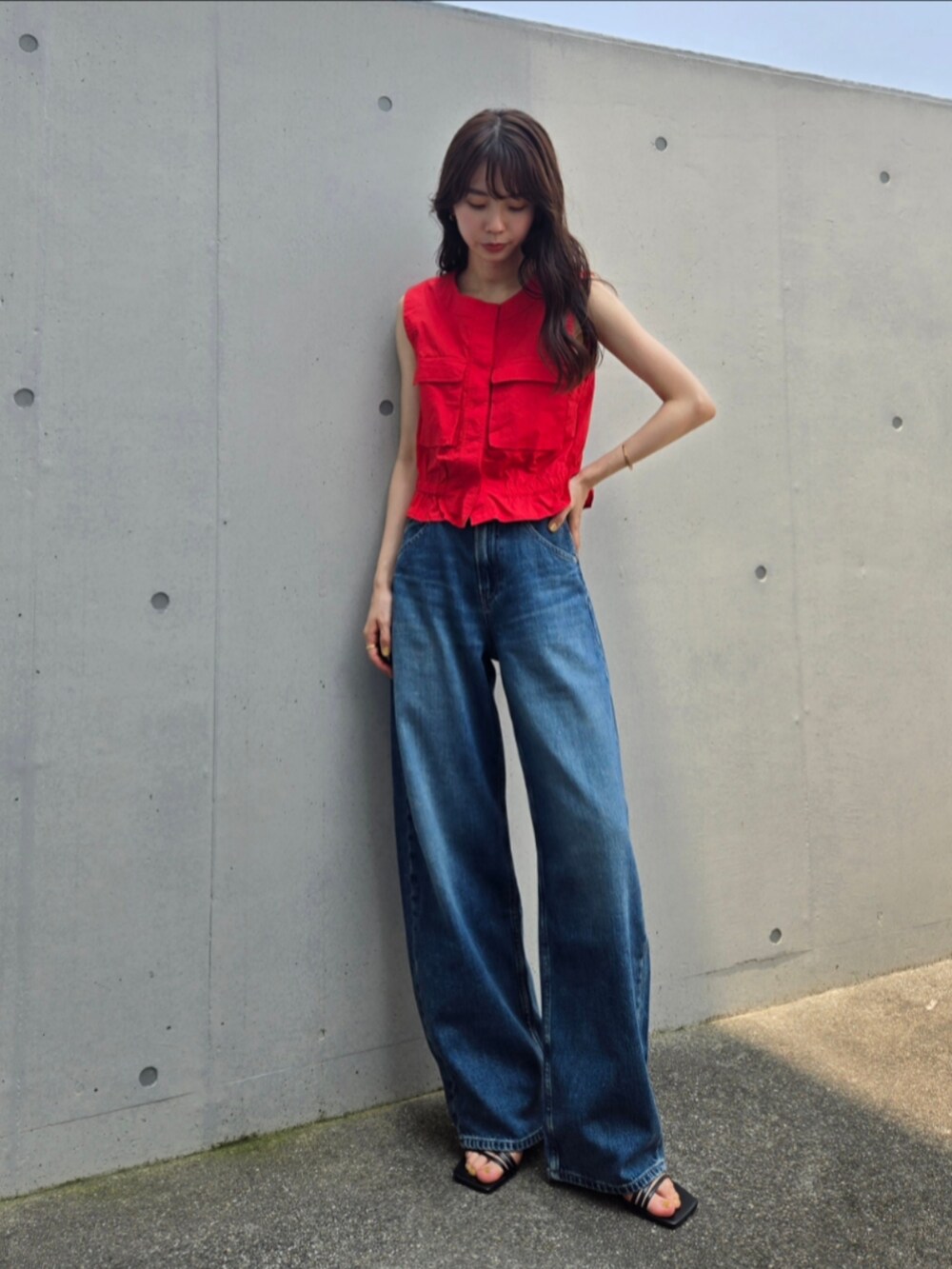 レッド系のベスト、ブルー系のデニムパンツ、ブラック系のサンダルを着用したレディースの夏コーディネートの3枚目の写真