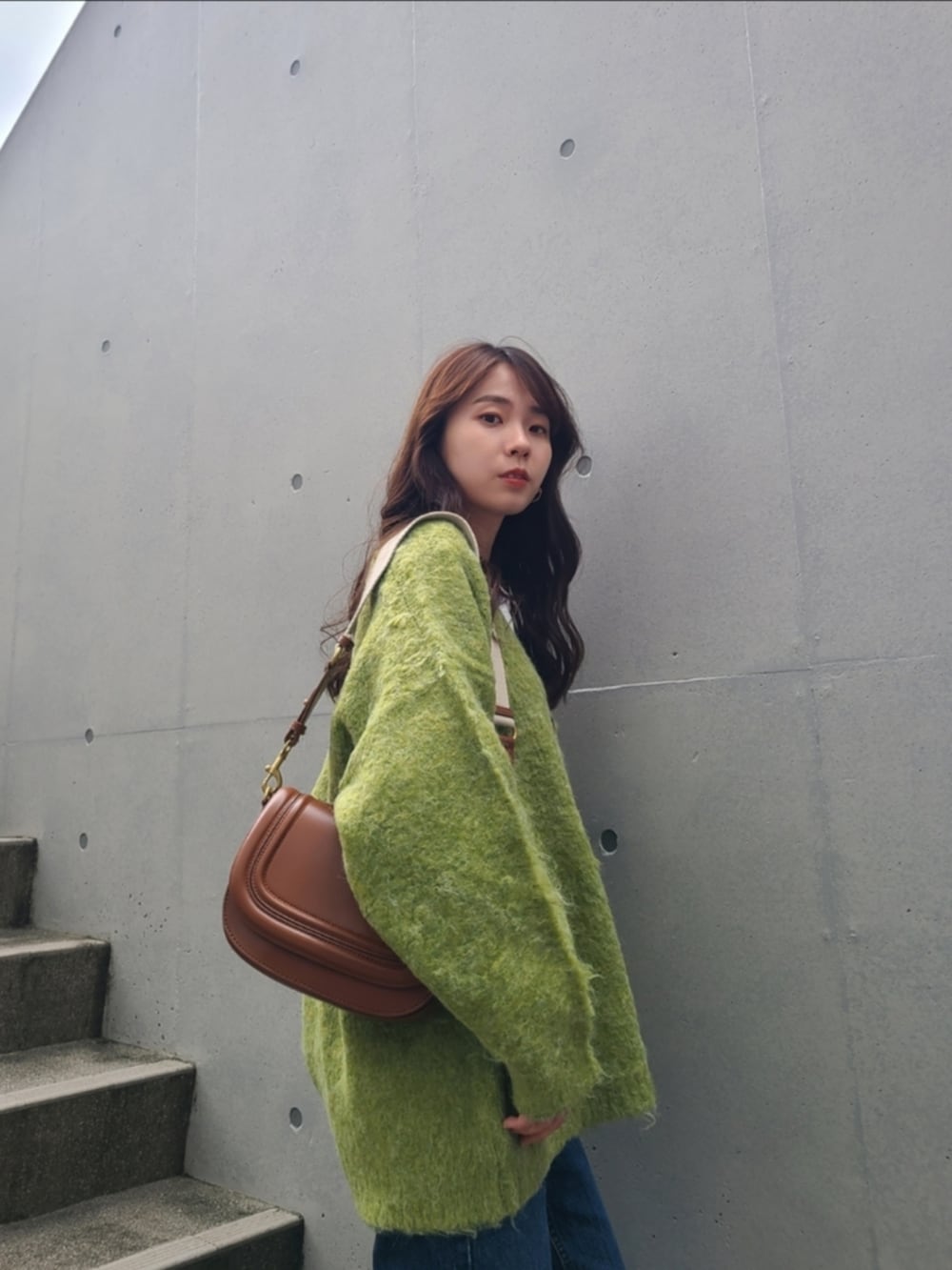 グリーン系のカーディガン/ボレロ、ブラウン系のバッグ、ブルー系のデニムパンツを着用したレディースの秋コーディネートの2枚目の写真