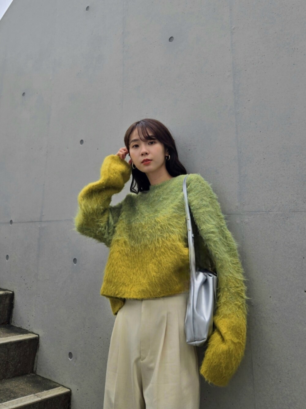 イエロー系のニット/セーター、シルバー系のハンドバッグ、ホワイト系のパンツを着用したレディースの秋コーディネートの2枚目の写真