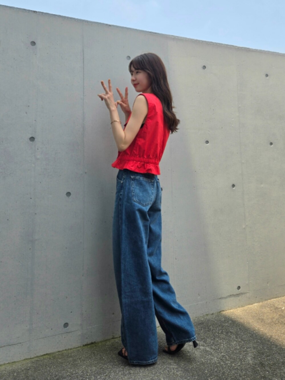 レッド系のベスト、ブルー系のデニムパンツ、ブラック系のサンダルを着用したレディースの夏コーディネートの2枚目の写真