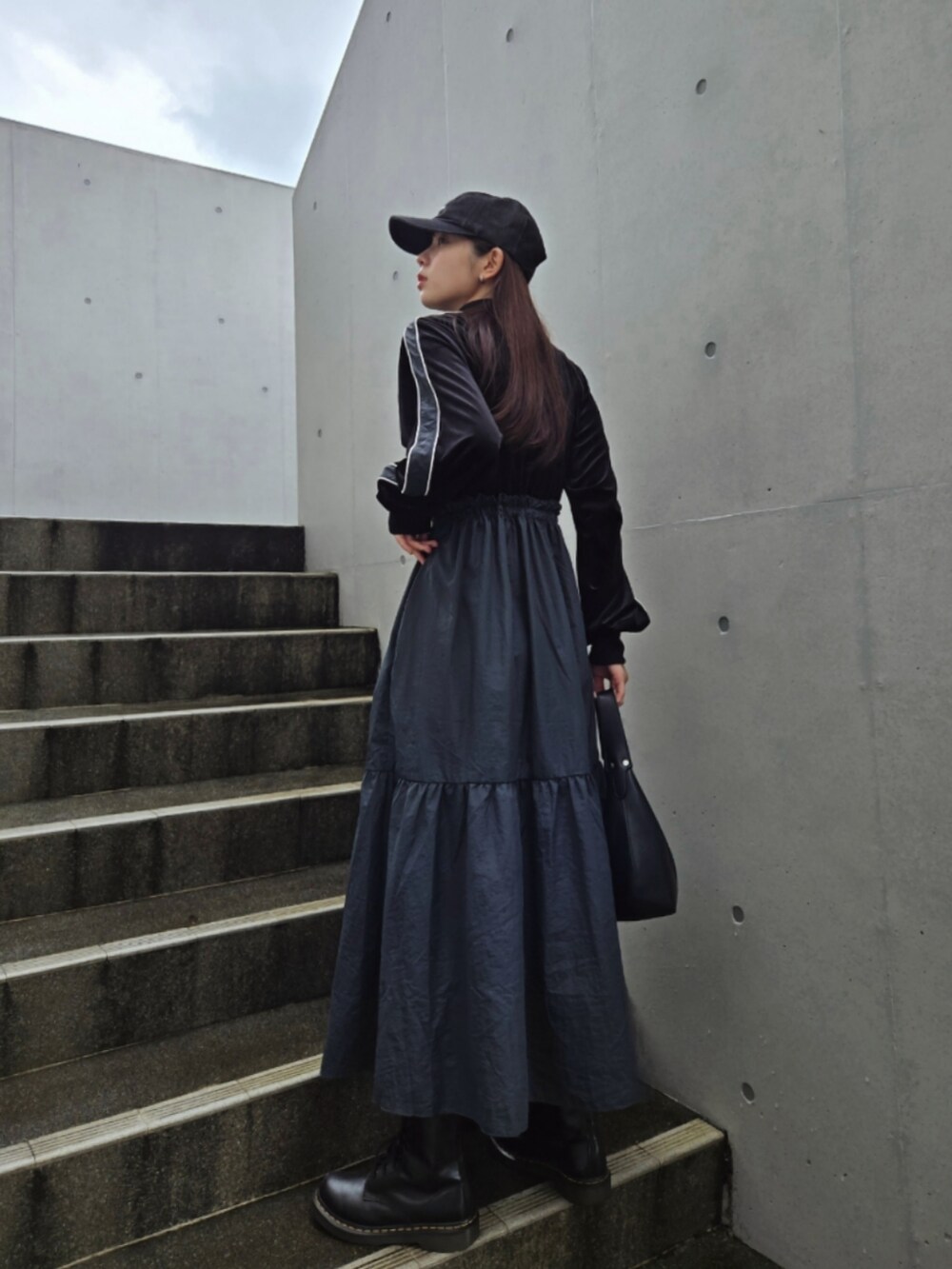 ブルー系のワンピース、ブラック系のブーツ、ブラック系のキャップを着用したレディースの秋コーディネートの2枚目の写真