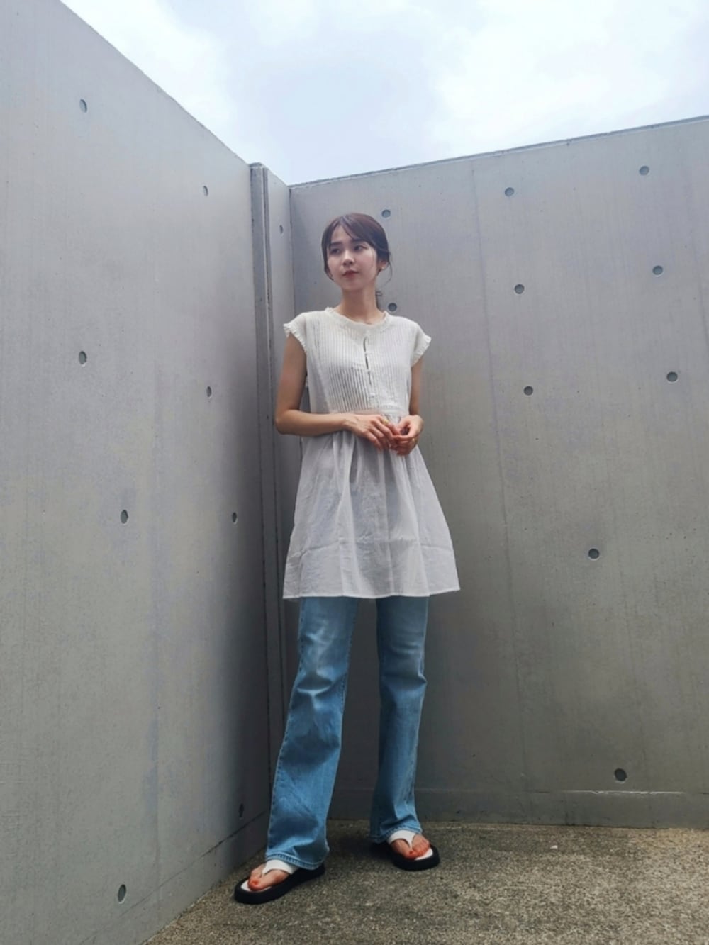 ブルー系のデニムパンツ、ホワイト系のチュニック、ホワイト系のサンダルを着用したレディースの夏コーディネートの2枚目の写真