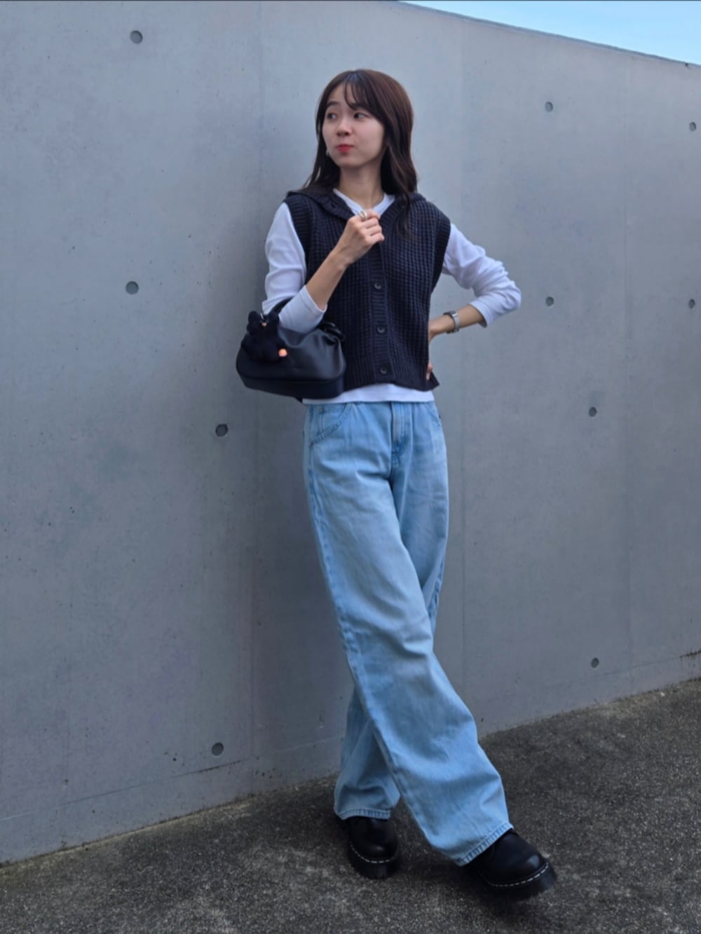 グレー系のニット/セーター、ブラック系のハンドバッグ、ブルー系のデニムパンツを着用したレディースの秋コーディネートの2枚目の写真