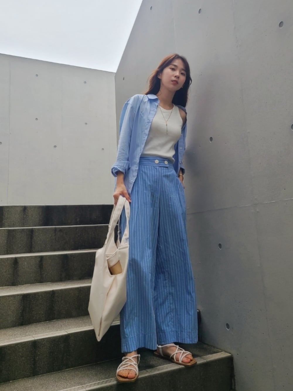 ブルー系のパンツ、ホワイト系のトップス、ホワイト系のサンダルを着用したレディースの夏コーディネートの2枚目の写真