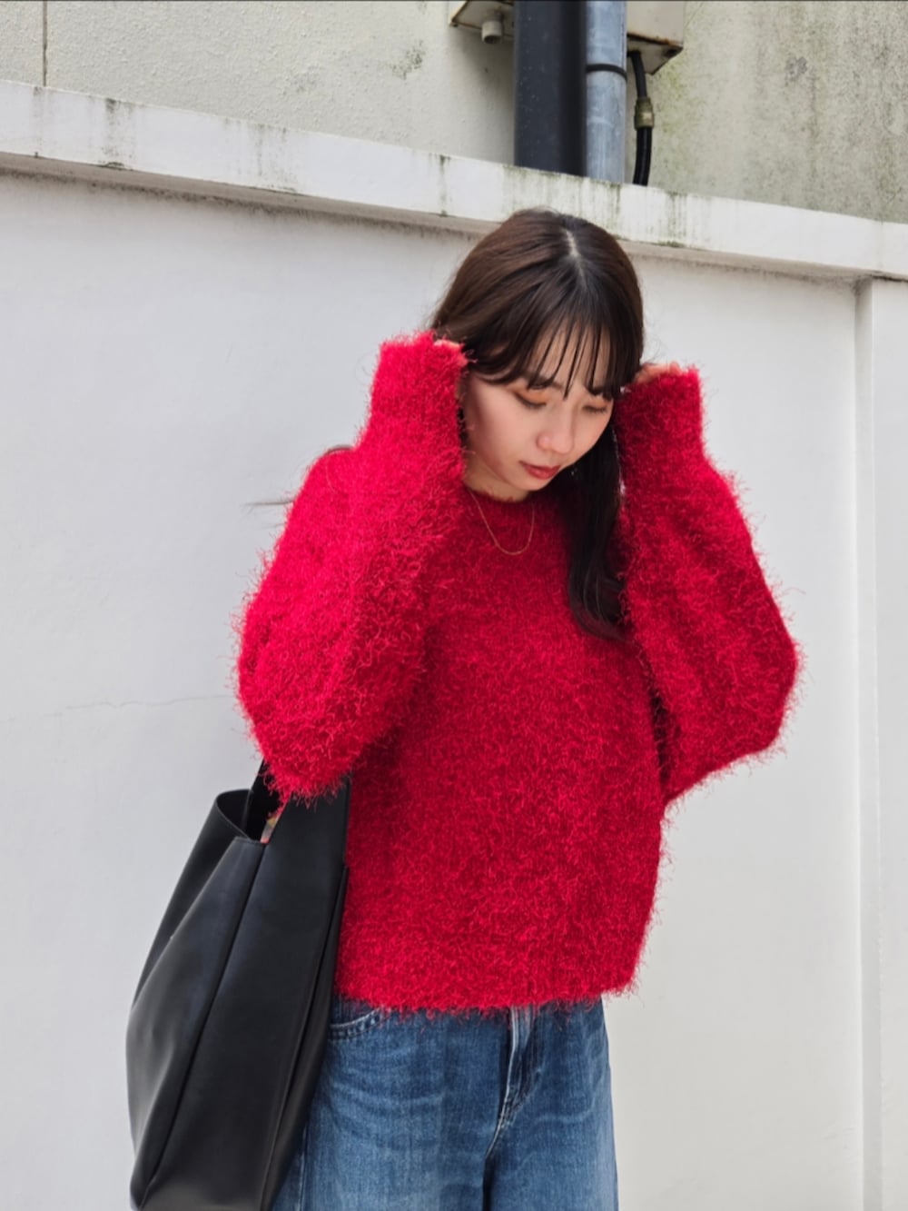 レッド系のニット/セーター、ブラック系のトートバッグ、ブルー系のデニムパンツを着用したレディースの秋コーディネートの3枚目の写真