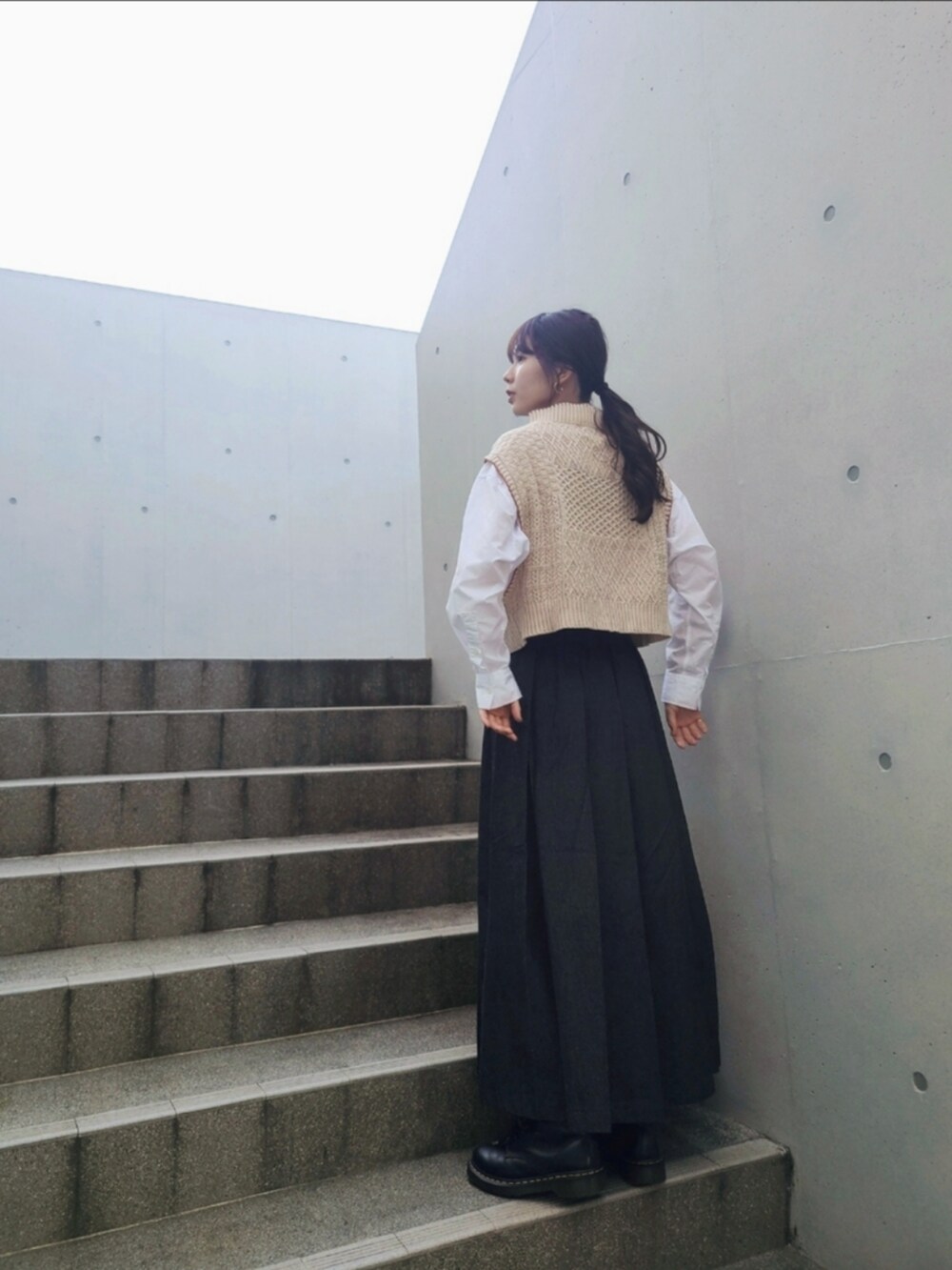 ベージュ系のベスト、ブラック系のデニムスカート、ブラック系のブーツを着用したレディースの秋コーディネートの2枚目の写真