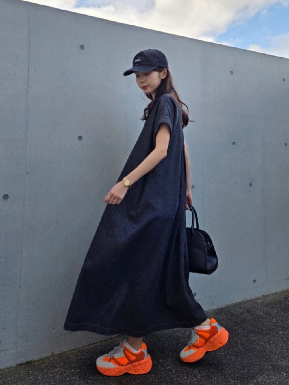 オレンジ系のスニーカー、ブラック系のボストンバッグ、ブラック系のワンピース/ドレスを着用したレディースの春コーディネートの2枚目の写真