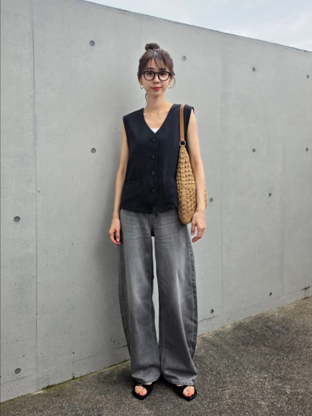 ブラック系のベスト、グレー系のデニムパンツ、ブラウン系のかごバッグを着用したレディースの夏コーディネートの2枚目の写真