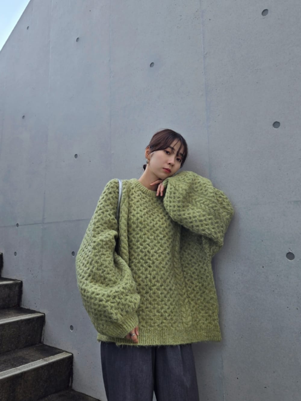 グリーン系のニット/セーター、グレー系のパンツ、シルバー系のハンドバッグを着用したレディースの秋コーディネートの2枚目の写真