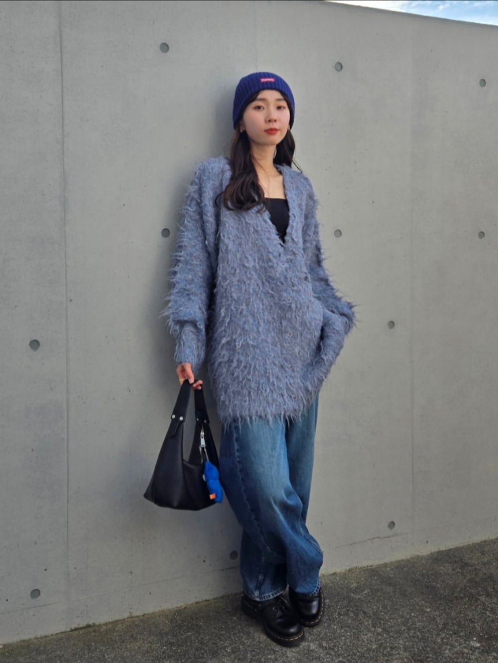 ブルー系のカーディガン/ボレロ、ブラック系のハンドバッグ、ブルー系のデニムパンツを着用したレディースの秋コーディネートの4枚目の写真