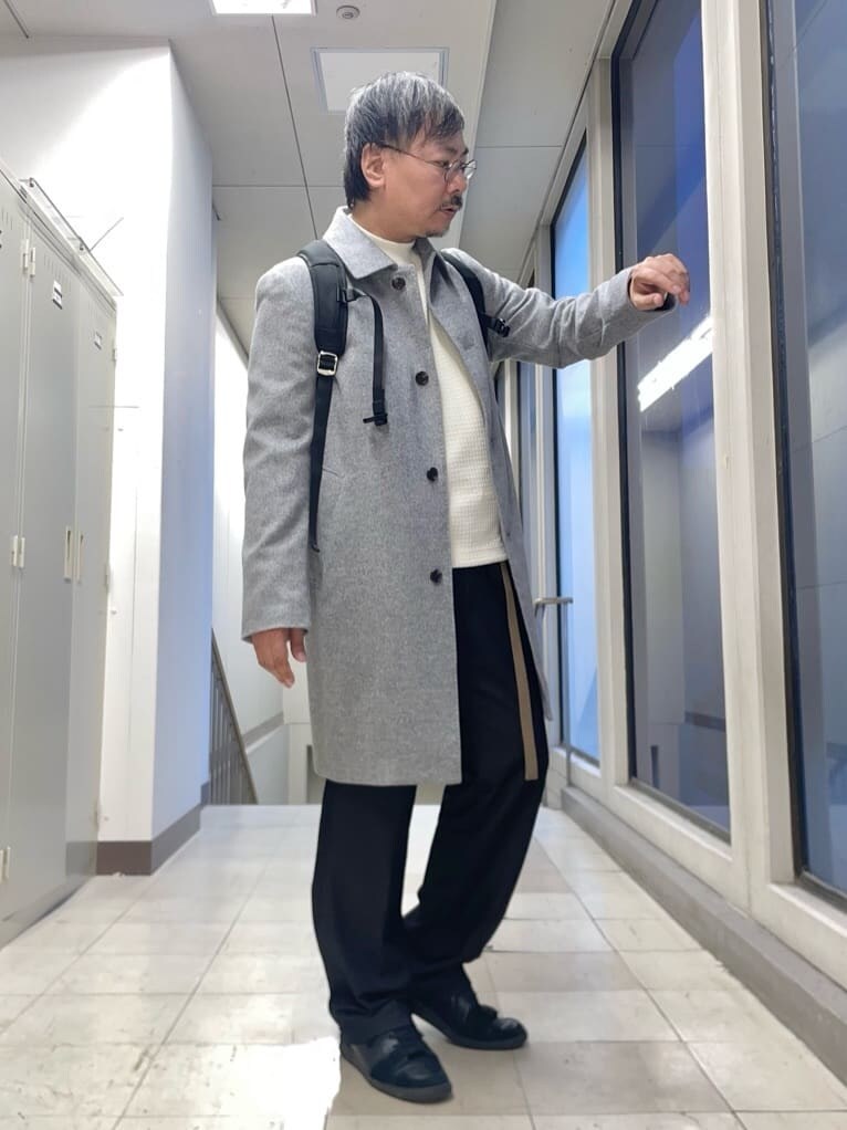 グレー系のステンカラーコート、ホワイト系のTシャツ/カットソー、ブラック系のバックパック/リュックを着用したメンズの秋コーディネートの5枚目の写真