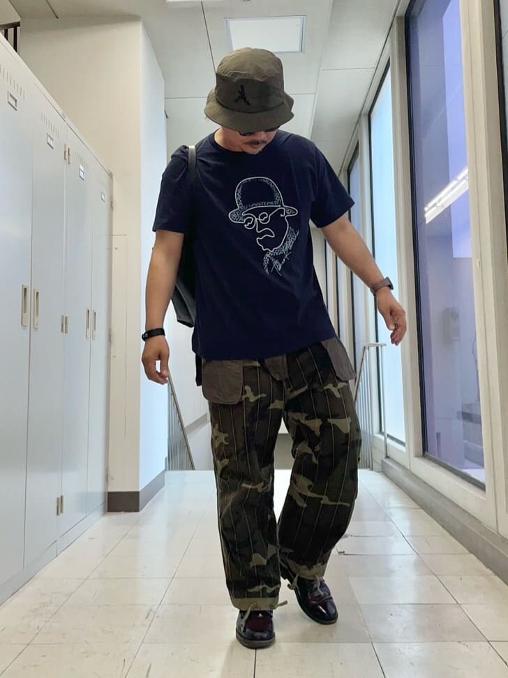 ブルー系のTシャツ/カットソー、ブラック系のトートバッグ、グリーン系のハットを着用したメンズの夏コーディネートの6枚目の写真