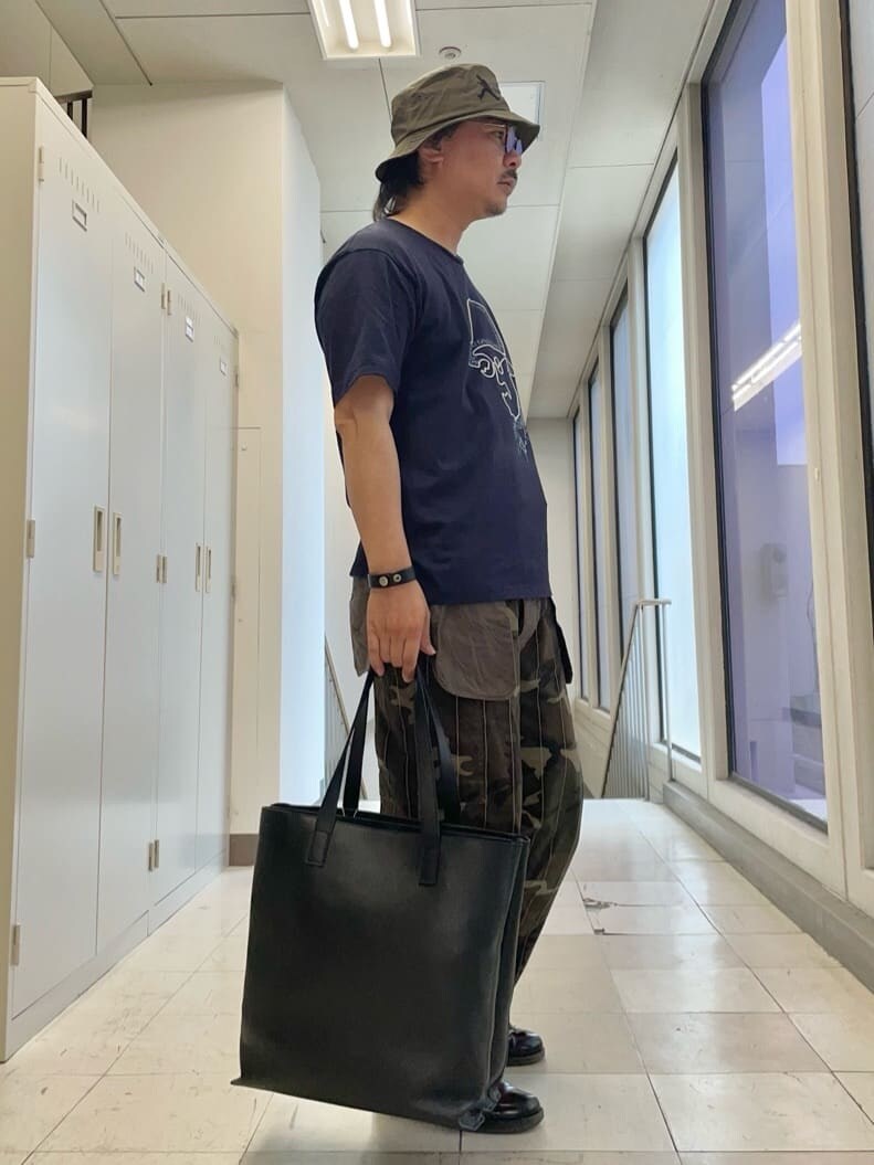 ブルー系のTシャツ/カットソー、ブラック系のトートバッグ、グリーン系のハットを着用したメンズの夏コーディネートの3枚目の写真