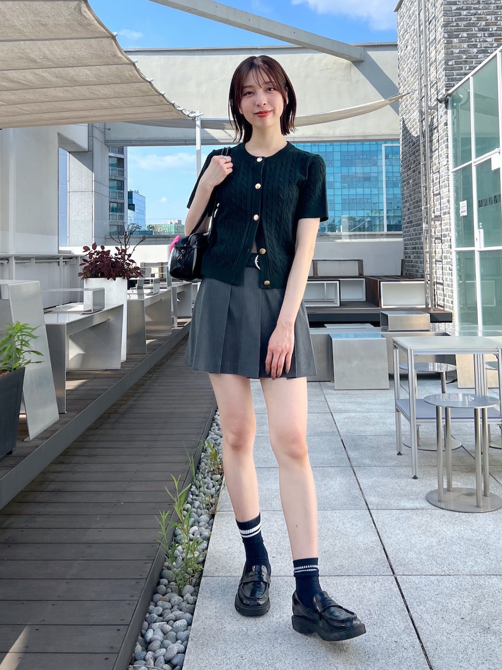 グレー系のスカート、グリーン系のカーディガン/ボレロ、ブラック系のローファーを着用したレディースの夏コーディネートの2枚目の写真