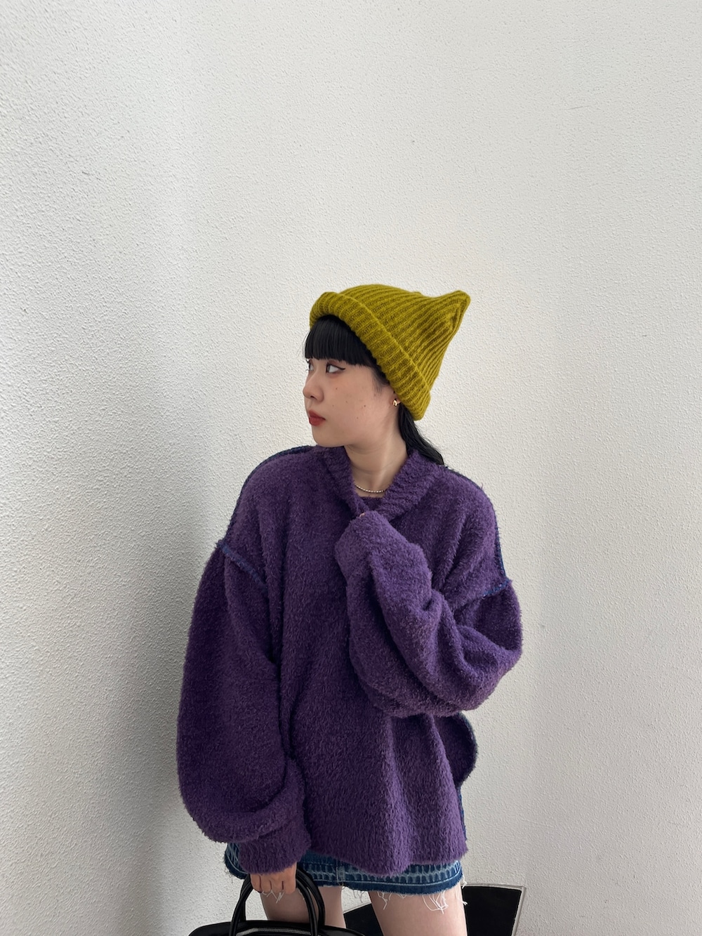 パープル系のニット/セーター、ブルー系のデニムパンツ、グリーン系のボストンバッグを着用したレディースの秋コーディネートの6枚目の写真