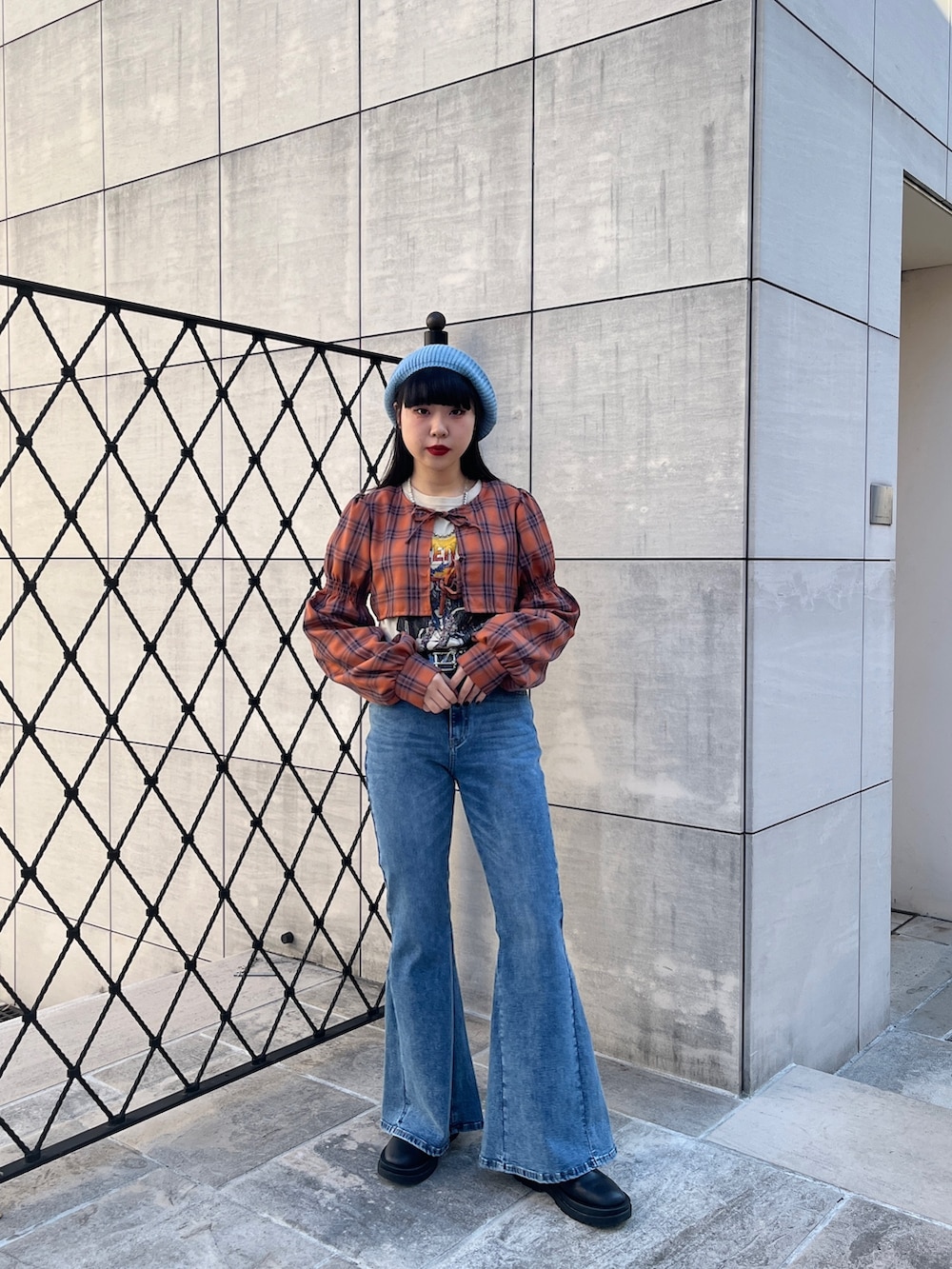 オレンジ系のワンピース、ブラック系のブーツ、ブルー系のデニムパンツを着用したレディースの冬コーディネートの2枚目の写真