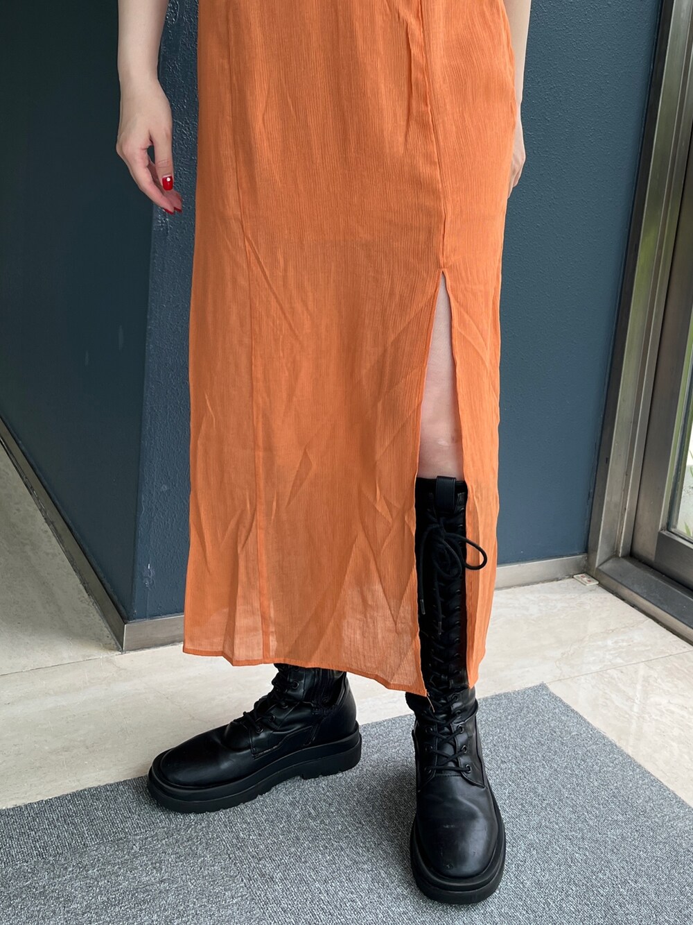 オレンジ系のワンピース、ホワイト系のTシャツ/カットソー、ブラック系のブーツを着用したレディースの夏コーディネートの7枚目の写真