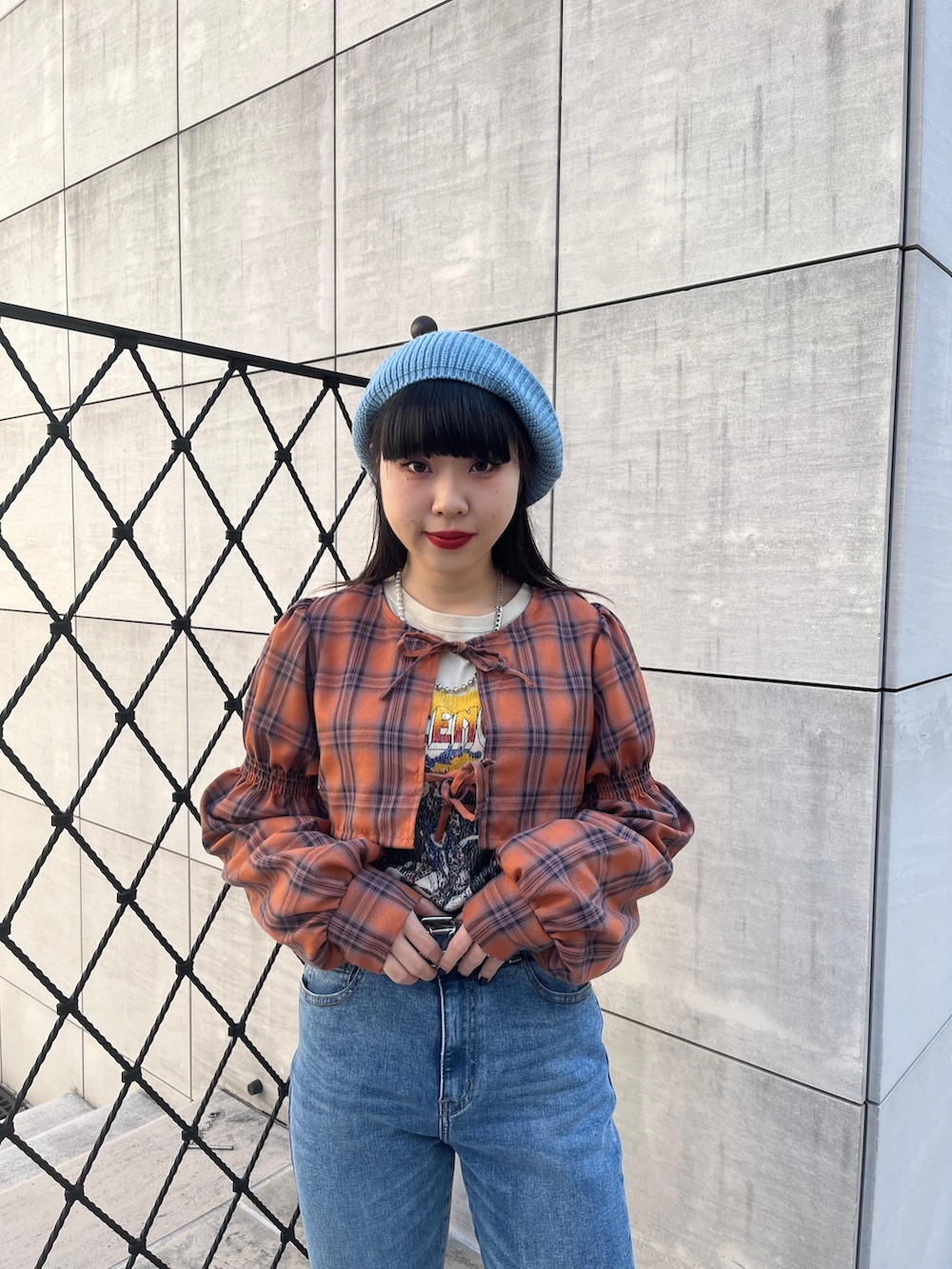 オレンジ系のワンピース、ブラック系のブーツ、ブルー系のデニムパンツを着用したレディースの冬コーディネートの5枚目の写真