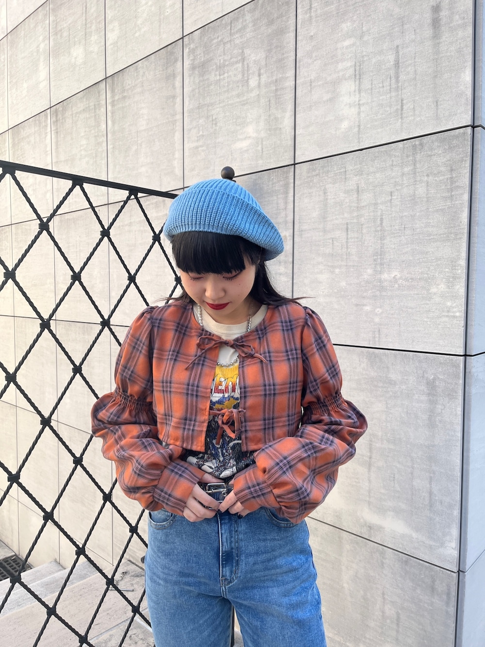 オレンジ系のワンピース、ブラック系のブーツ、ブルー系のデニムパンツを着用したレディースの冬コーディネートの4枚目の写真