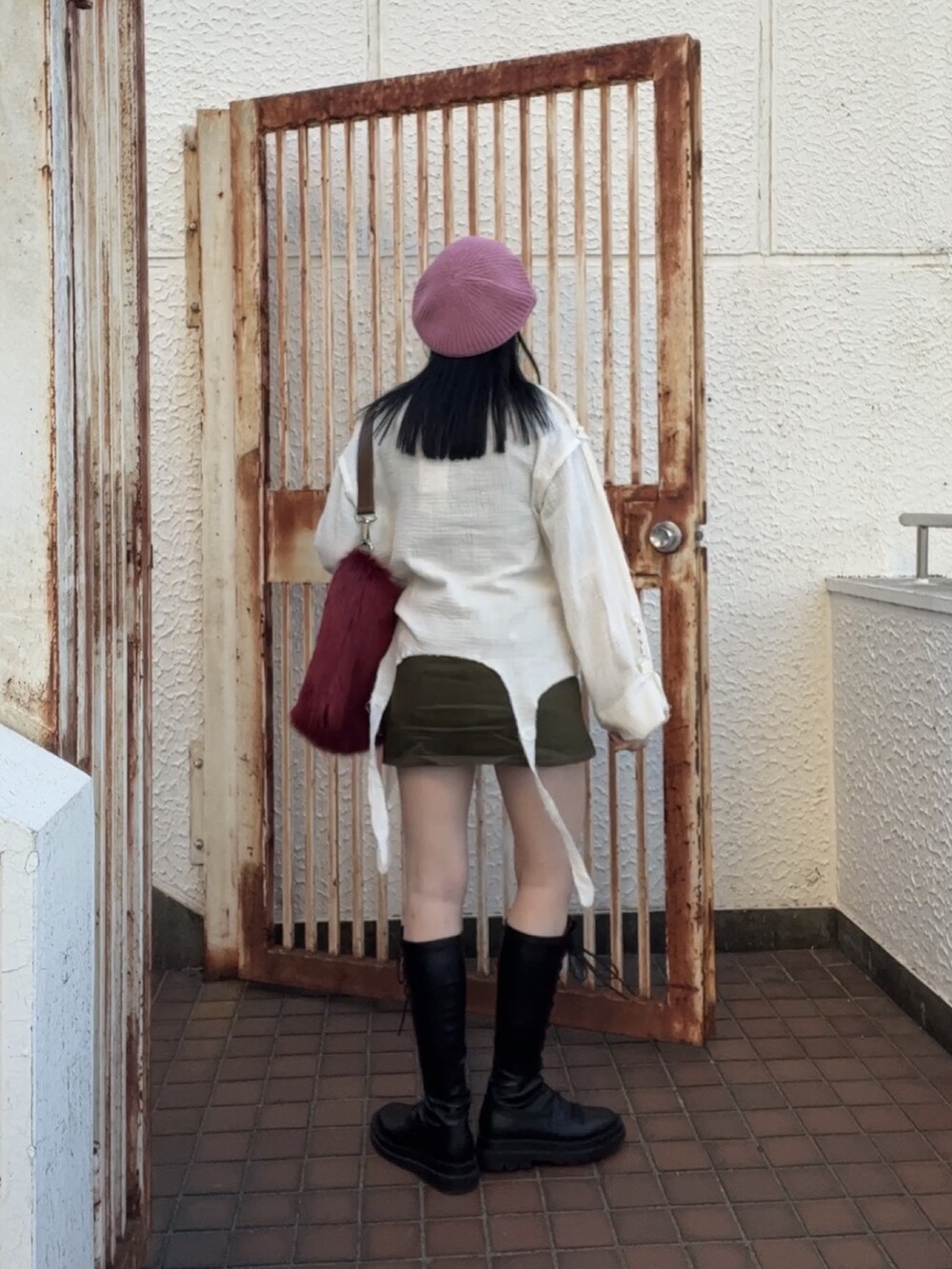 ブラック系のスカート、ブラック系のブーツ、レッド系のショルダーバッグを着用したレディースの冬コーディネートの4枚目の写真