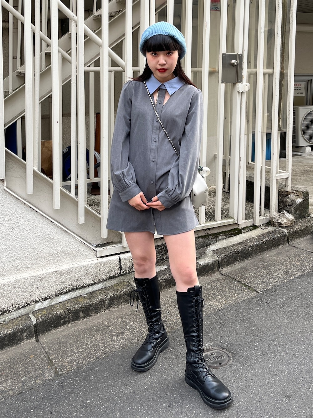 グレー系のワンピース、ブラック系のブーツ、ホワイト系のショルダーバッグを着用したレディースの冬コーディネートの2枚目の写真