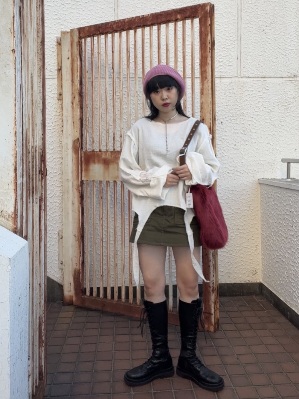 ブラック系のスカート、ブラック系のブーツ、レッド系のショルダーバッグを着用したレディースの冬コーディネートの2枚目の写真