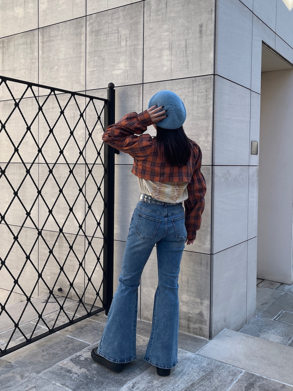 オレンジ系のワンピース、ブラック系のブーツ、ブルー系のデニムパンツを着用したレディースの冬コーディネートの3枚目の写真