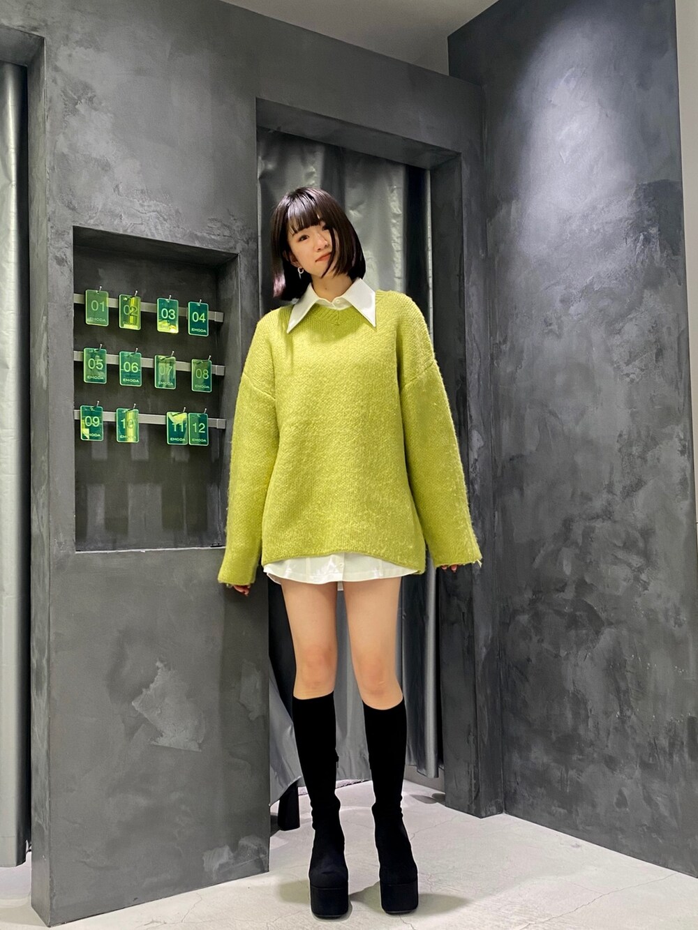 ブラック系のブーツ、イエロー系のニット/セーター、ホワイト系のワンピースを着用したレディースの冬コーディネートの2枚目の写真