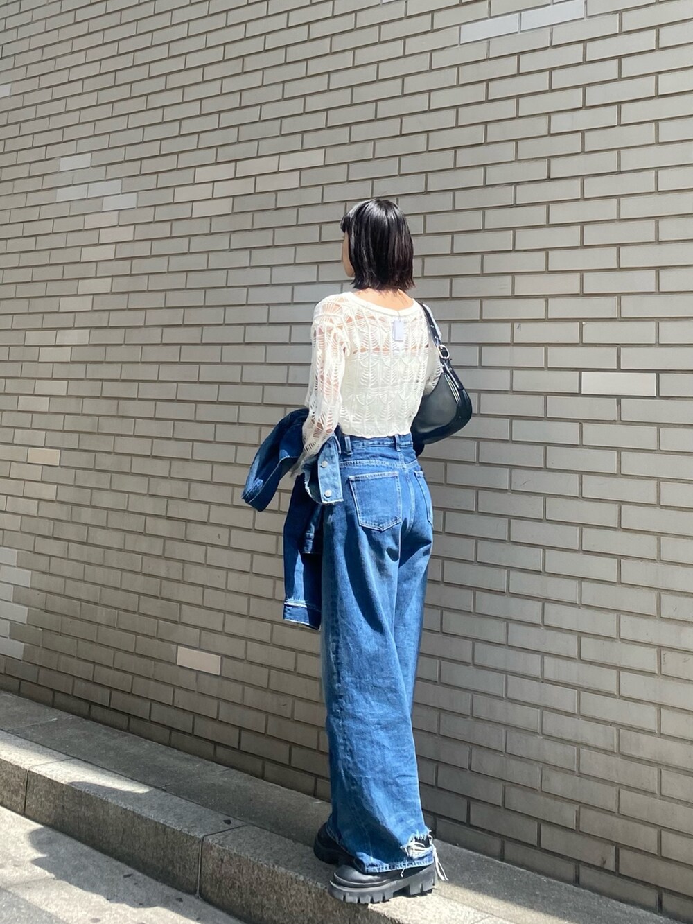 ブラック系のブーツ、ブラック系のハンドバッグ、ブルー系のデニムパンツを着用したレディースの春コーディネートの6枚目の写真