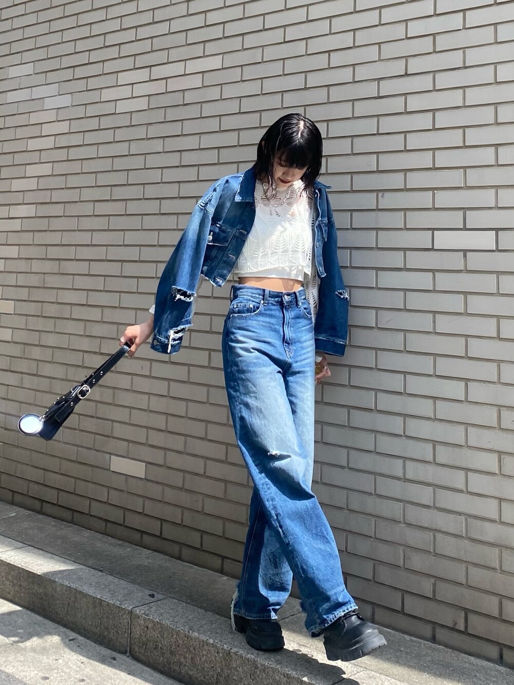 ブラック系のブーツ、ブラック系のハンドバッグ、ブルー系のデニムパンツを着用したレディースの春コーディネートの2枚目の写真