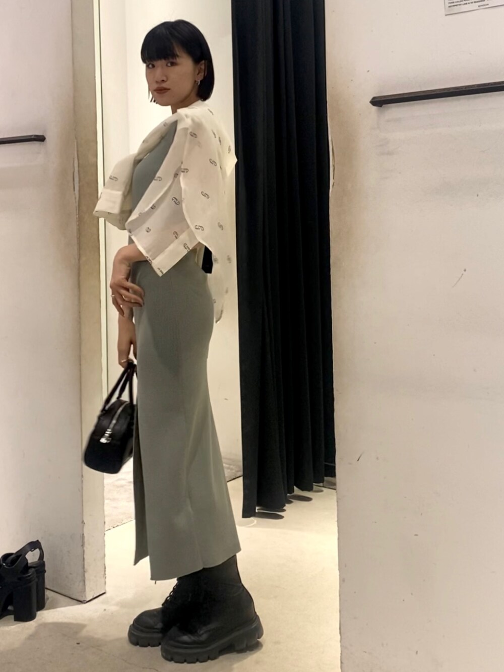 ブラック系のハンドバッグ、ブラック系のブーツ、グレー系のワンピースを着用したレディースの春コーディネートの2枚目の写真