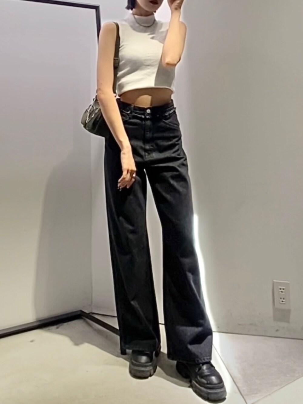 ブラック系のデニムパンツ、ブラック系のブーツ、グリーン系のハンドバッグを着用したレディースの夏コーディネートの3枚目の写真