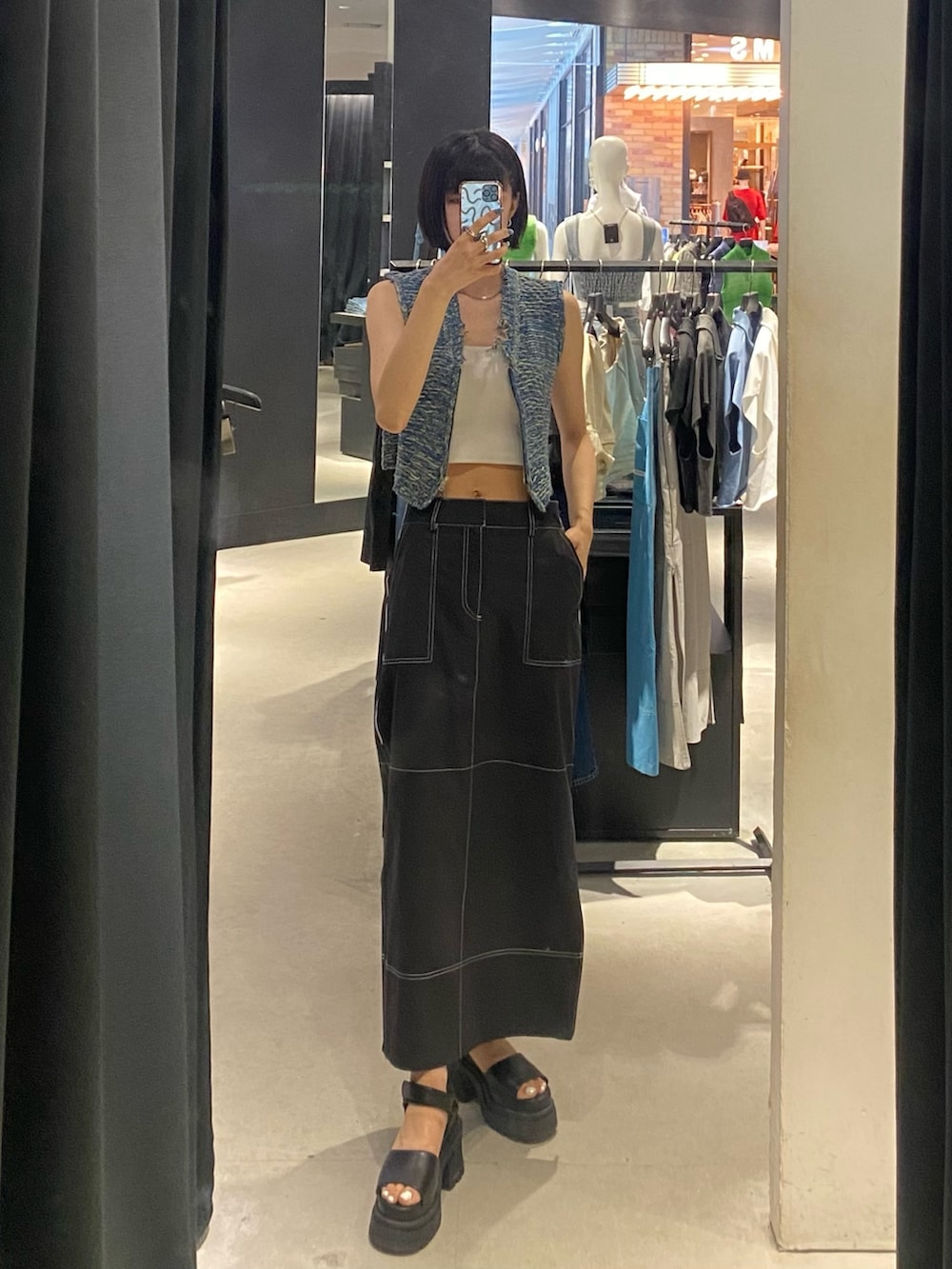 ブラック系のサンダル、ブラック系のスカート、ブルー系のベストを着用したレディースの夏コーディネートの2枚目の写真