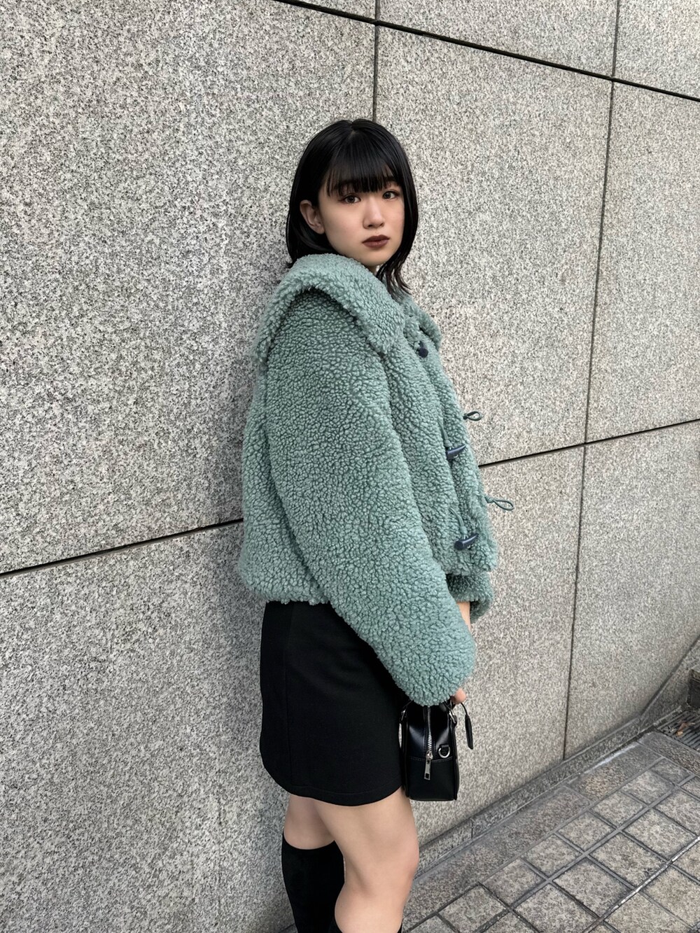 グリーン系のブルゾン、ブラック系のスカート、その他のブーツを着用したレディースの冬コーディネートの6枚目の写真