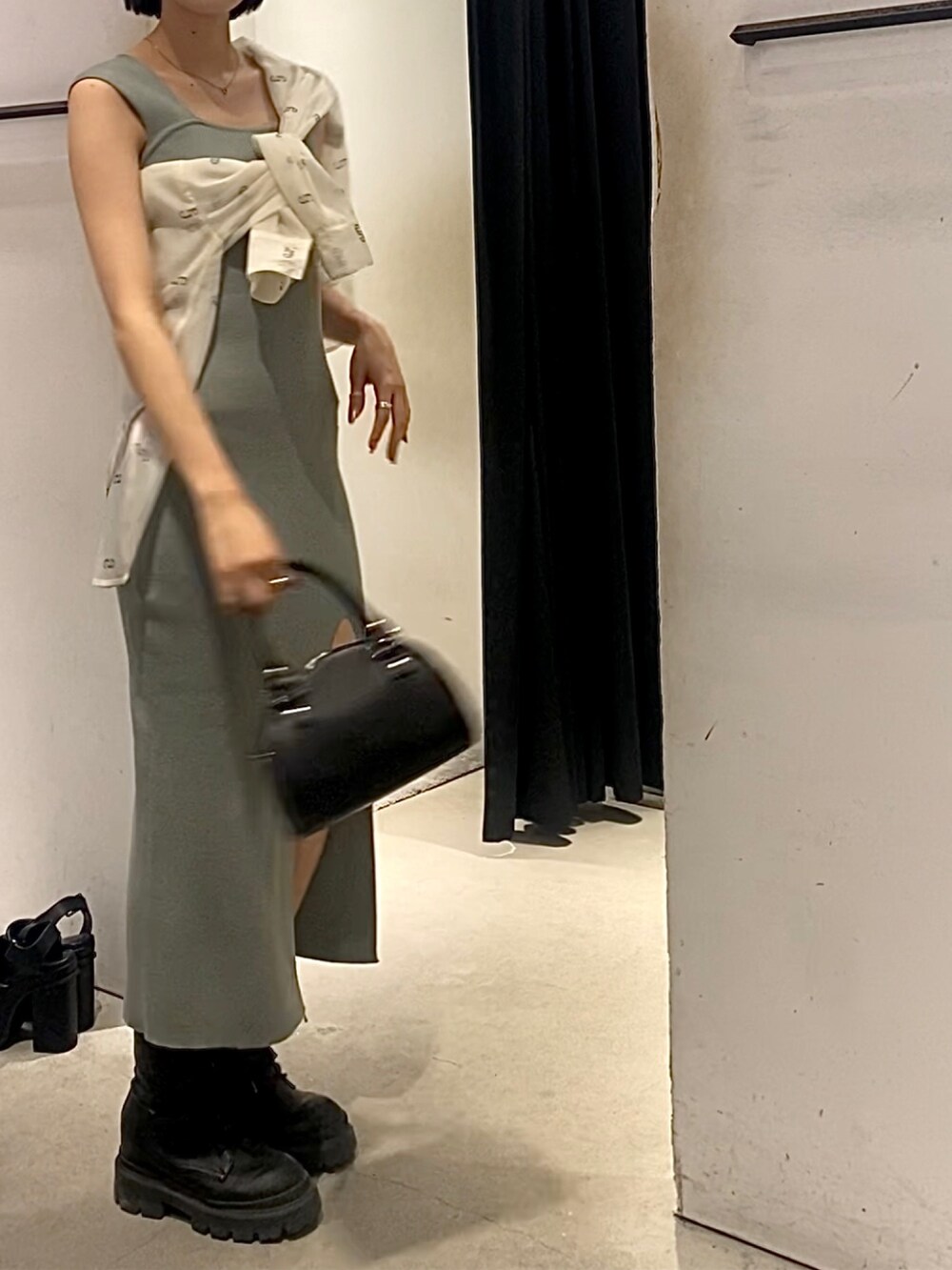 ブラック系のハンドバッグ、ブラック系のブーツ、グレー系のワンピースを着用したレディースの春コーディネートの3枚目の写真