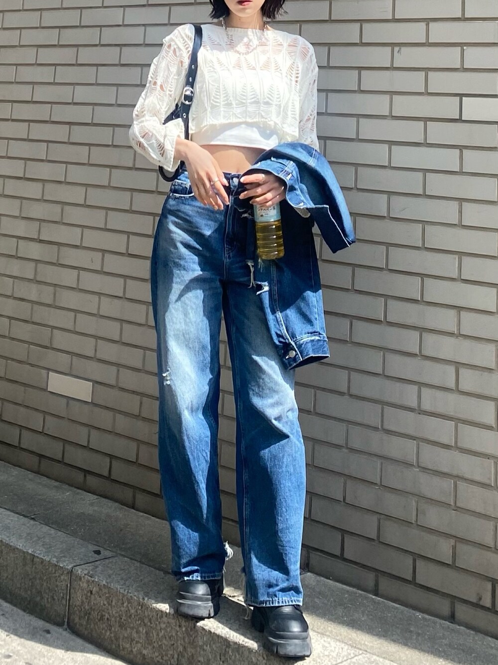 ブラック系のブーツ、ブラック系のハンドバッグ、ブルー系のデニムパンツを着用したレディースの春コーディネートの5枚目の写真