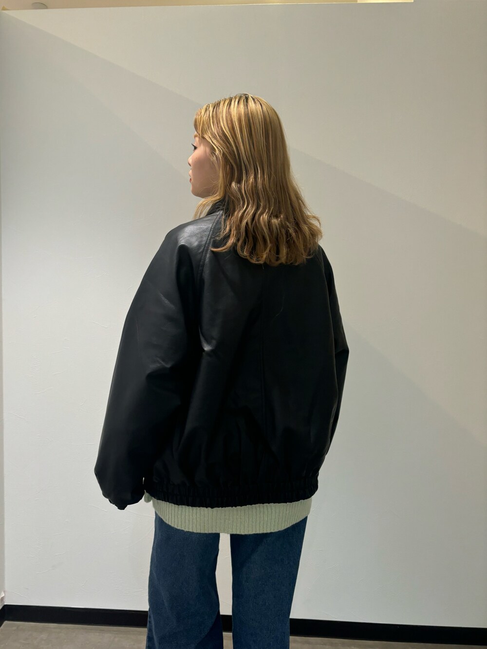 ブラック系のブルゾン、グリーン系のニット/セーター、ブルー系のデニムパンツを着用したレディースの秋コーディネートの4枚目の写真