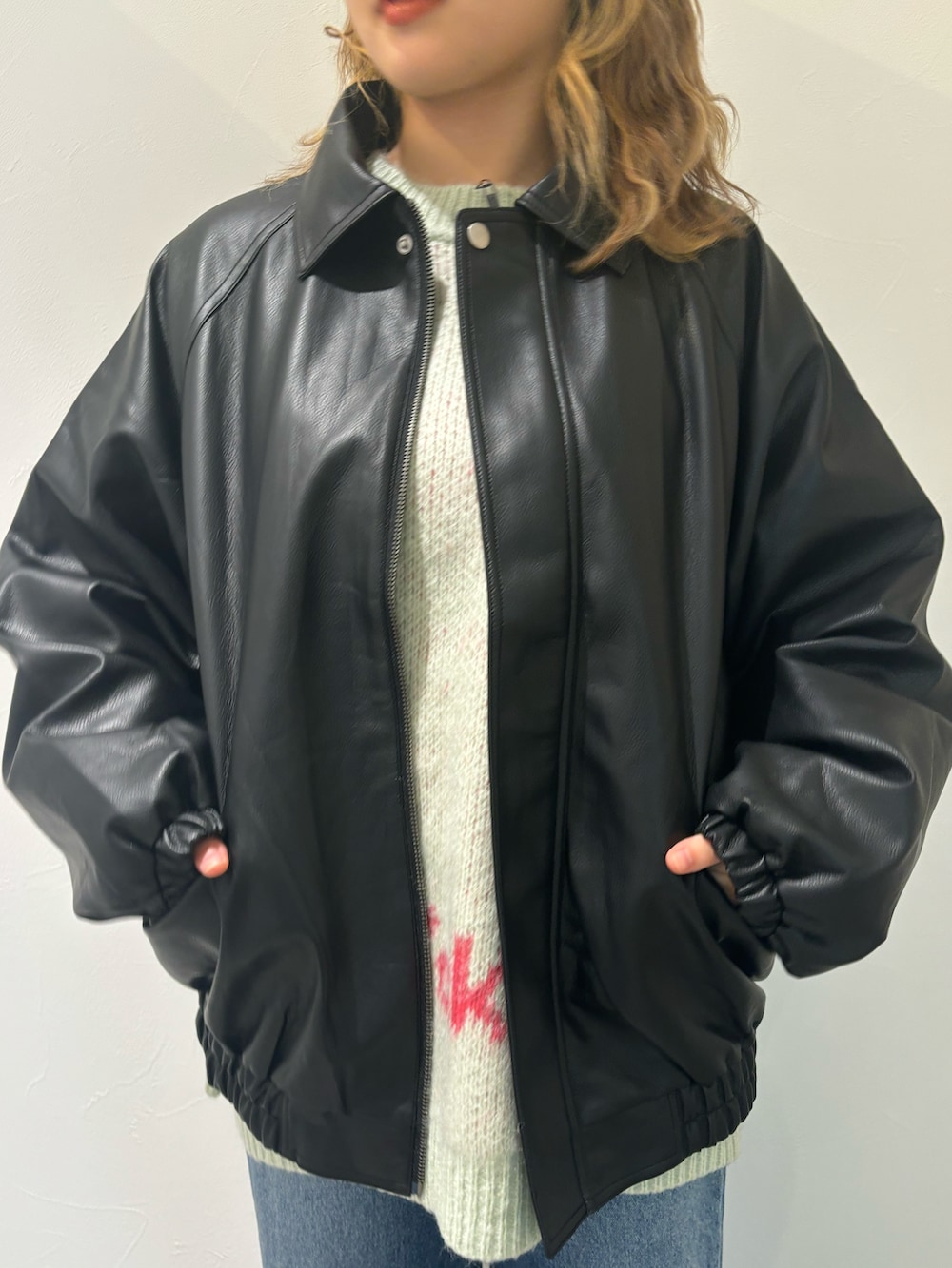 ブラック系のブルゾン、グリーン系のニット/セーター、ブルー系のデニムパンツを着用したレディースの秋コーディネートの3枚目の写真