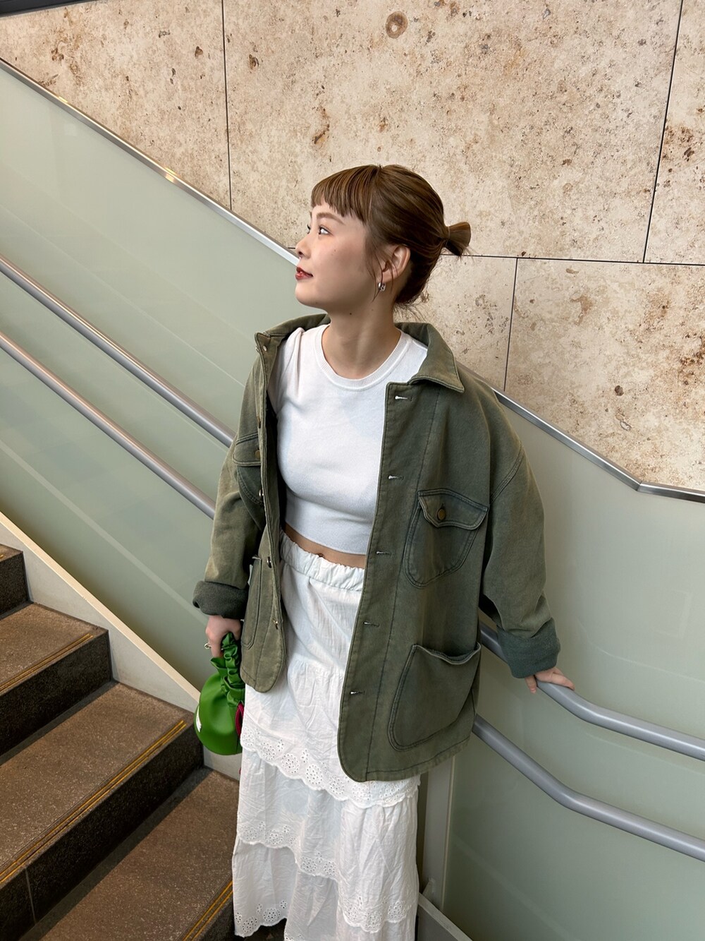 ホワイト系のスカート、グリーン系のカバーオール、グリーン系のハンドバッグを着用したレディースの冬コーディネートの2枚目の写真