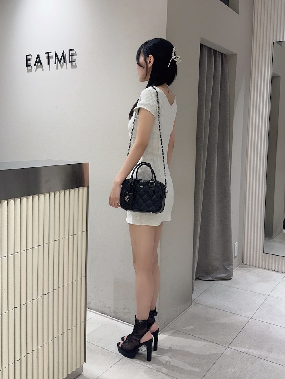 ホワイト系のワンピース、ブラック系のハンドバッグ、ブラック系のサンダルを着用したレディースの夏コーディネートの2枚目の写真
