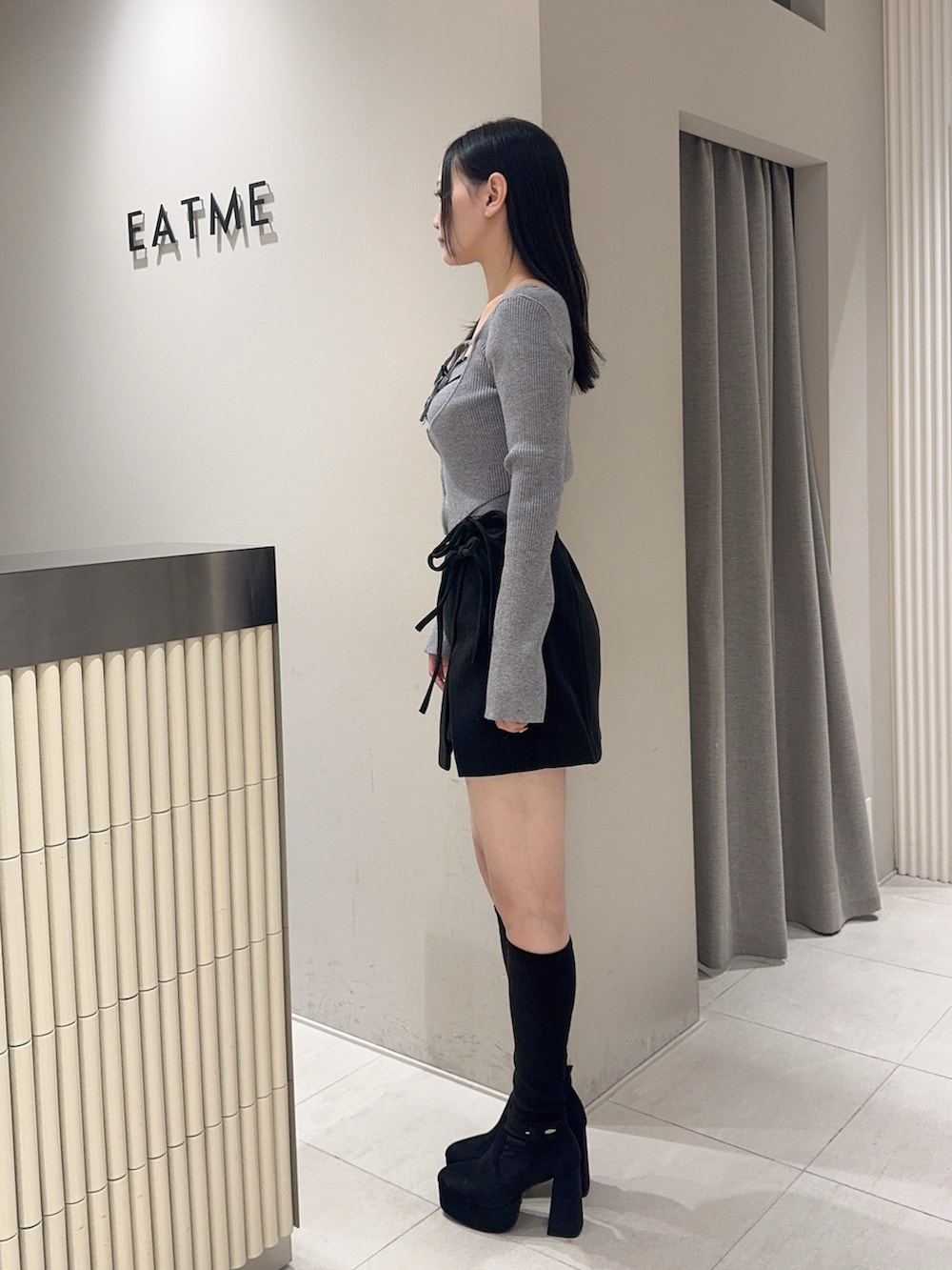 グレー系のニット/セーター、ブラック系のスカート、ブラック系のブーツを着用したレディースの秋コーディネートの2枚目の写真